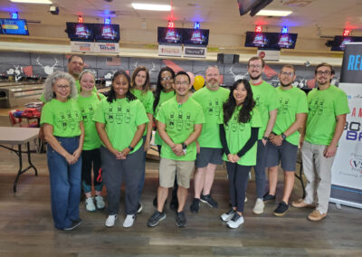 A group of 12 people posing for a group photo, wearing green Amputee Bowler Bash t-shirts.