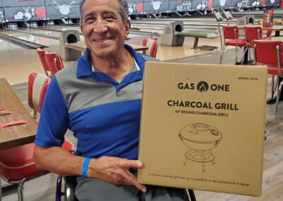 A man in a wheelchair smiling, holding a charcoal grill in a box.