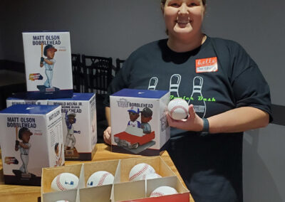 A woman showing off multiple Matt Olson bobbleheads, baseballs, and a baseball bat.