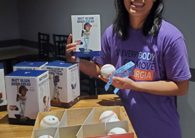 A woman holding a Matt Olson Bobblehead box, a baseball, and raffle tickets.