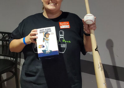 A woman holding a Matt Olson Bobblehead box, a baseball bat, and a baseball.