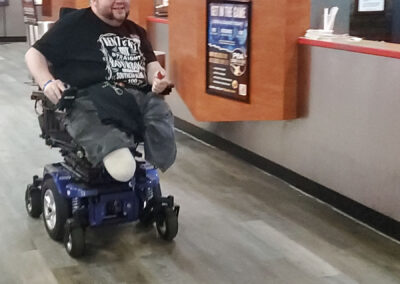 A man in a wheelchair and missing legs riding around in the bowling alley.