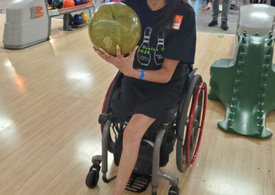 A woman in a wheelchair smiling with a bowling ball in hand.