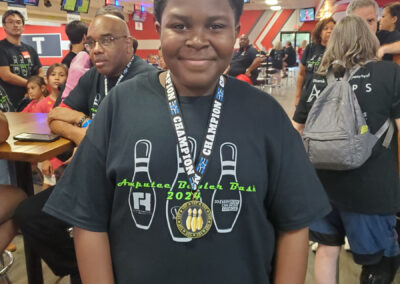 A young boy wearing a Champion medal and a Amputee Bowler Bash t-shirt.