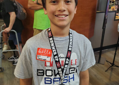 A young boy wearing a Runner Up medal and a Amputee Bowler Bash t-shirt.