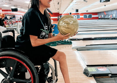 A woman with a missing leg and in a wheelchair bowling, smiling.