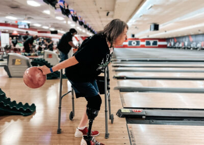 A female wearing a leg prosthetic about to bowl a ball down a lane.