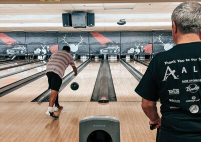 A man with a prosthetic throwing a bowling ball while another man watches.