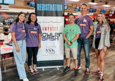 Five attendees standing by a poster that advertises the Amputee Bowler Bash, presented by Vascular Surgical Atlanta Prosthetics.