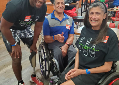 Two people in wheelchairs smiling with a man wearing a prosthetic leg.